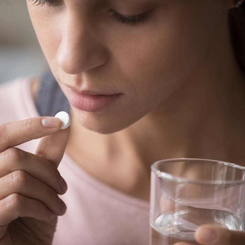 Frau mit Wasserglas in der Hand nimmt eine Tablette