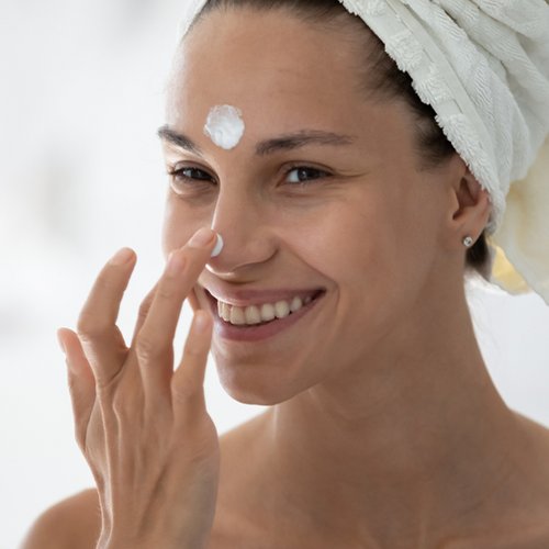 Lächelnde Frau trägt nach der Dusche Gesichtspflege auf