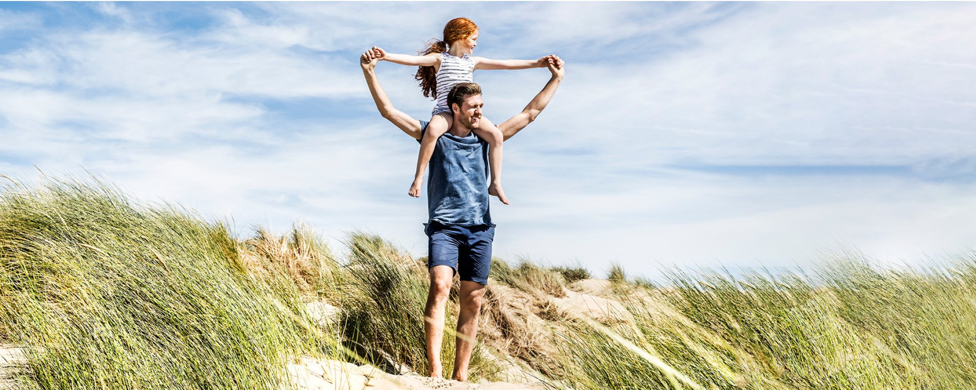 Sunny beach scene, father carrying his daughter on his shoulders