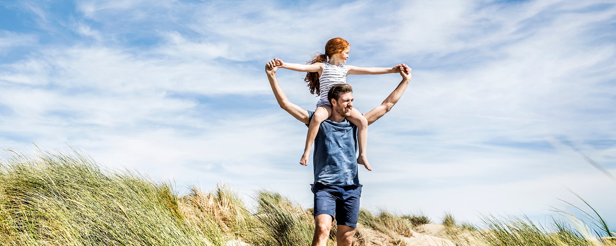 Sunny beach scene, father carrying his daughter on his shoulders