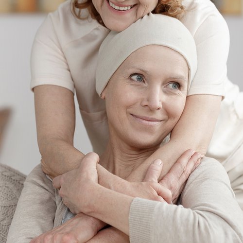 Lächelnde Krebspatientin wird von Frau umarmt