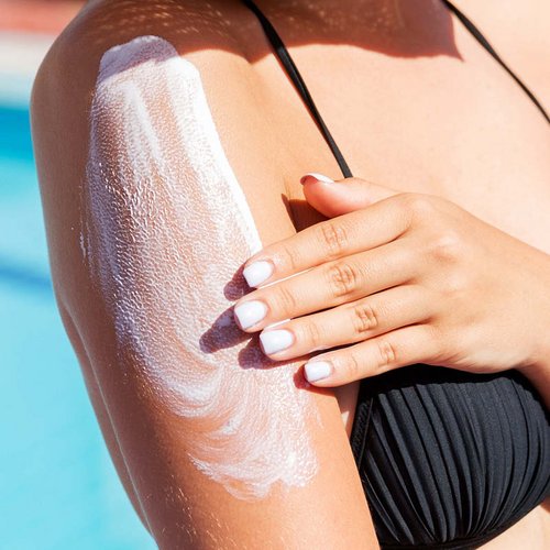 Eine Frau am Pool trägt Sonnenschutz auf ihrem Oberarm auf.Eine Frau am Pool trägt Sonnenschutz auf ihrem Oberarm auf.