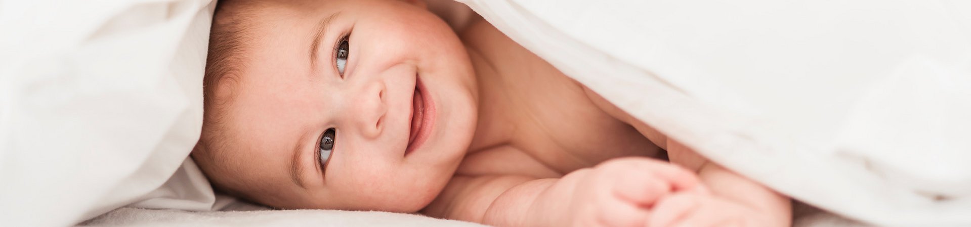 [Translate to Niederländisch:] Lächelndes Baby unter einer weißen Decke