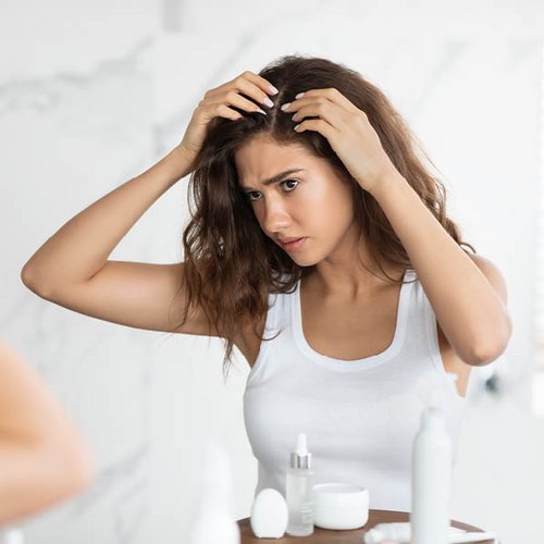Eine junge Frau untersucht ihren Haaransatz auf Schuppen.