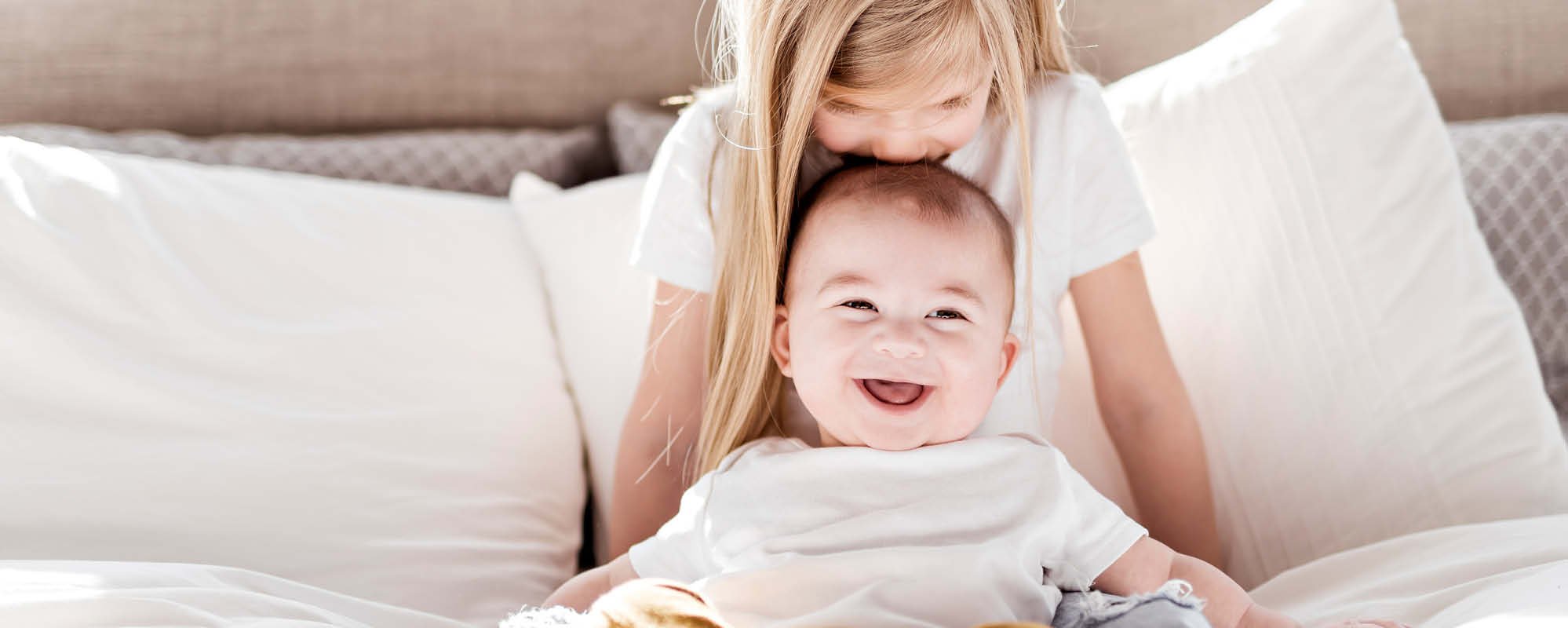 Blonde girl kisses her baby brother on the head